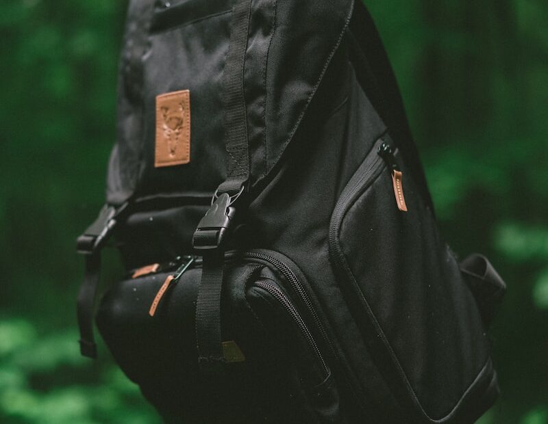 selective focus photo of black backpack hanging on brown tree branch
